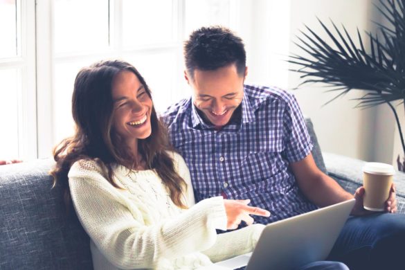 mężczyzna i kobieta siedzący na sofie śmieją się wskazując palcem na ekran laptopa