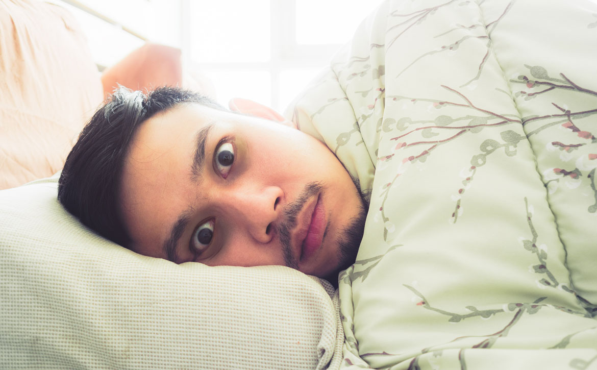 mężczyzna w łóżku z szeroko otwartymi oczami