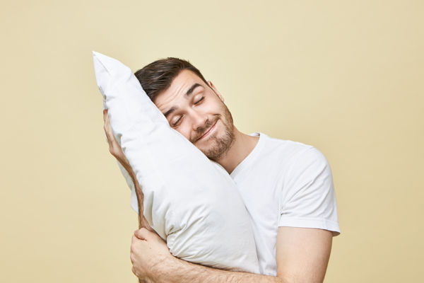 młody uśmiechnięty mężczyzna próbujący szybko zasnąć z poduszką na stojąco